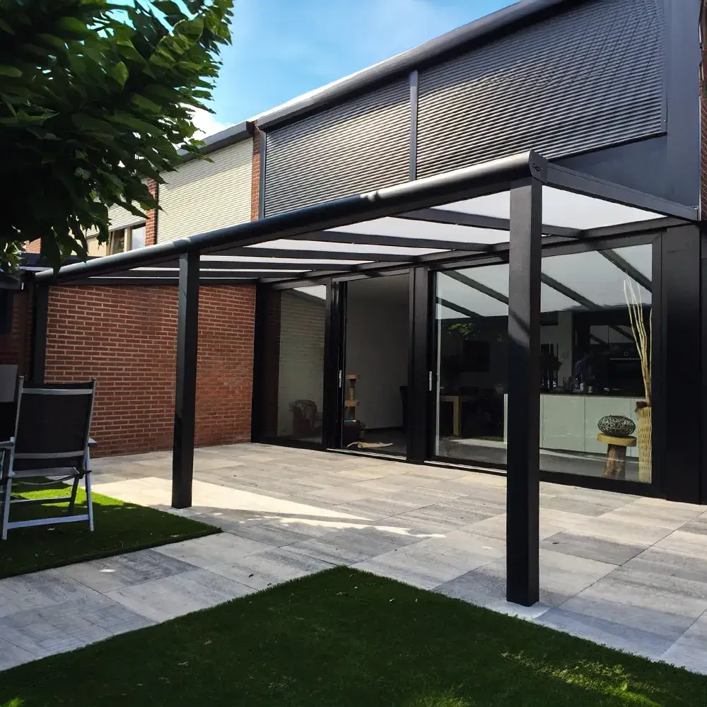 Antraciet aluminium veranda aan het huis gemonteerd, met strakke bestrating en weelderig groen gras.