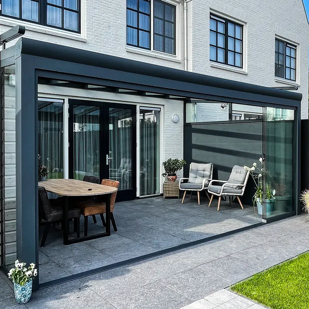 Glazen veranda aan huis met zonwering, uitkijkend op een verzorgde tuin met een stijlvolle tuinset.